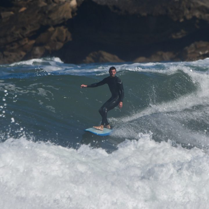 El surfista, de pie sobre la tabla, abre los brazos en la ola.