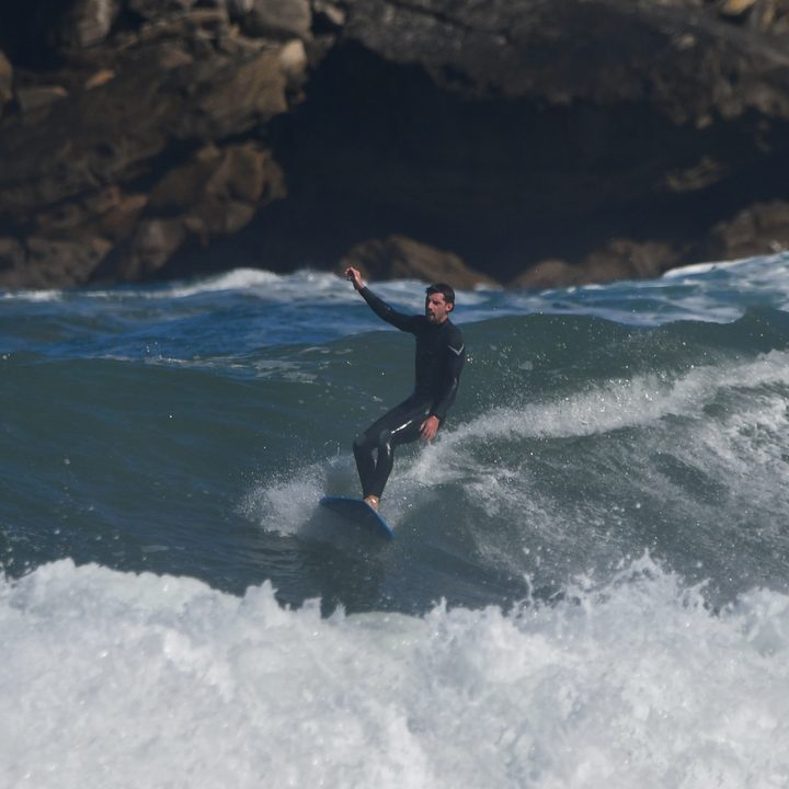 El surfista levanta un brazo mientras la ola rompe a su lado.