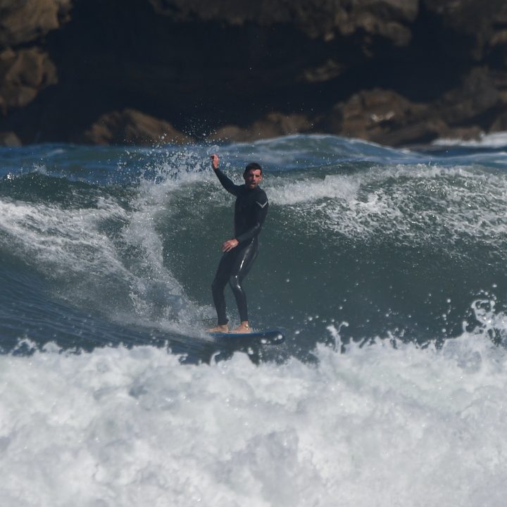 El surfista sigue de pie en la ola, con el brazo en alto.
