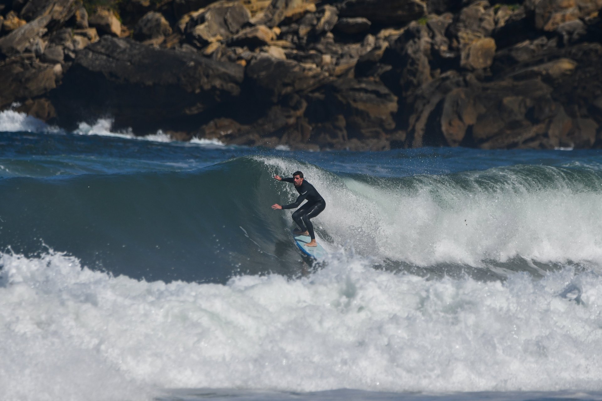 Un surfista en una ola de la Zurriola, con las rocas de la costa al fondo.